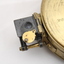 Gold coloured metal compass case with engraved lid; compass face is green printed paper with glass top.