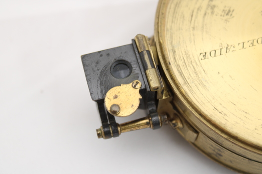 Gold coloured metal compass case with engraved lid; compass face is green printed paper with glass top.