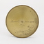 Gold coloured metal compass case with engraved lid; compass face is green printed paper with glass top.