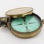 Gold coloured metal compass case with engraved lid; compass face is green printed paper with glass top.