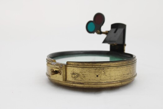 Gold coloured metal compass case with engraved lid; compass face is green printed paper with glass top.