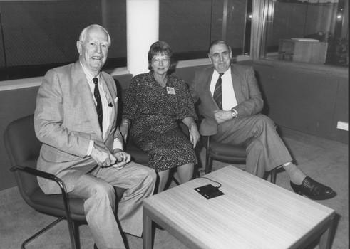 Three people seated in a meeting room looking towards camera