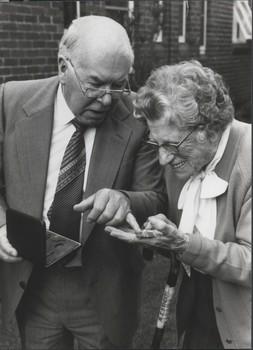 Older man points to medal held by elderly woman