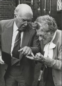 Older man points to medal held by elderly woman