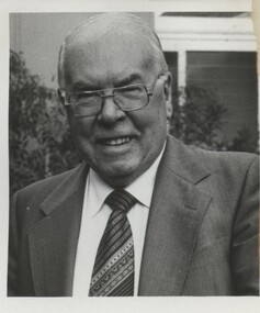 Older man with suit and tie smiles towards camera