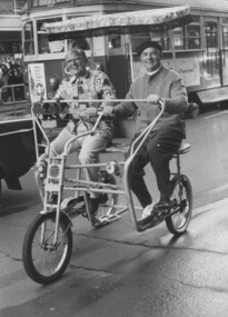 Two men riding a tricycle in city streets