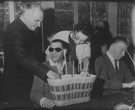 Man wearing glasses speaks with man and woman standing next to him who are feeling the cane work