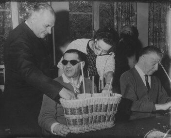 Man wearing glasses speaks with man and woman standing next to him who are feeling the cane work