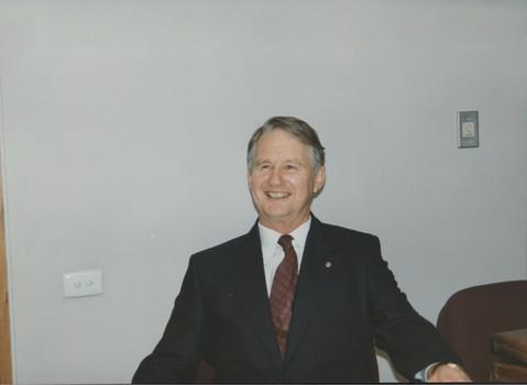 Man smiling as he sits at table, wearing suit and tie