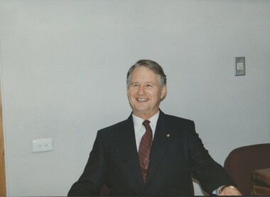 Man smiling as he sits at table, wearing suit and tie
