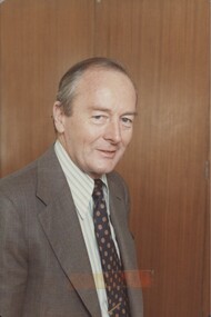 Portrait of man with suit, tie and striped shirt half turned towards camera