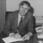 Suited man smiles towards camera as he writes in a diary