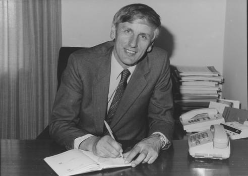 Suited man smiles towards camera as he writes in a diary