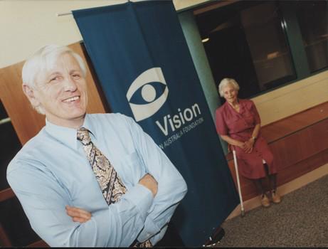 John Cook stands in front of VAF banner with older woman sitting on ledge behind him