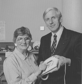John Cook holding a large button telephone for a woman