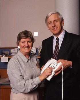 John Cook holding a large button telephone for a woman