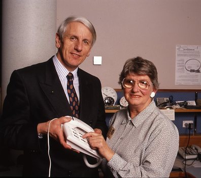 John Cook holding a large button telephone for a woman