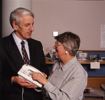 John Cook holding a large button telephone for a woman