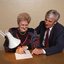 John Cook sitting next to a woman writing on a thickly lined notepad