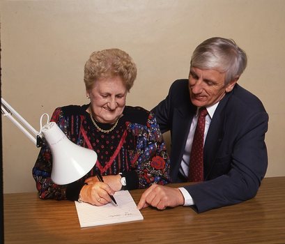 John Cook sitting next to a woman writing on a thickly lined notepad