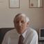 John Cook sitting in his office chair with framed certificates behind him