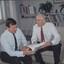 Two men sit on lounge chairs looking at paperwork and smiling 