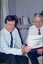 Two men sit on lounge chairs looking at paperwork and smiling 