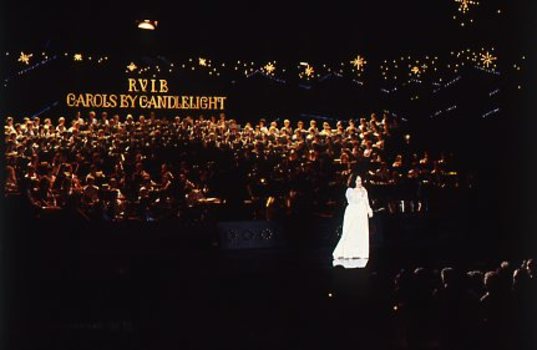 Stella Axarlis in white dress sings to crowd whilst behind her the choir and band perform