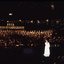 Stella Axarlis in white dress sings to crowd whilst behind her the choir and band perform