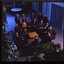 15 people sit around a small table and turn towards the photographer who is a floor above them