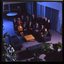 15 people sit around a small table and turn towards the photographer who is a floor above them