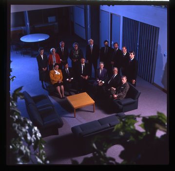 15 people sit around a small table and turn towards the photographer who is a floor above them