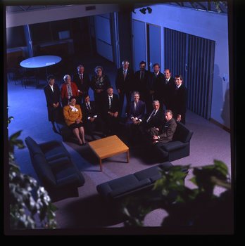 15 people sit around a small table and turn towards the photographer who is a floor above them