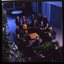 15 people sit around a small table and turn towards the photographer who is a floor above them