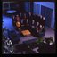 15 people sit around a small table and turn towards the photographer who is a floor above them