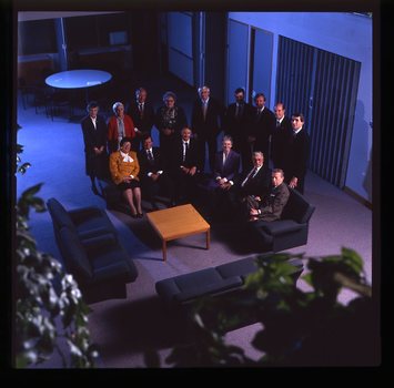 15 people sit around a small table and turn towards the photographer who is a floor above them