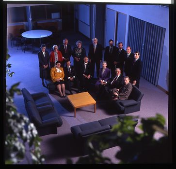 15 people sit around a small table and turn towards the photographer who is a floor above them