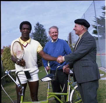 Bill Cosby dressed for tennis shaking Hubert Opperman's hand whilst Arthur Wilkins looks on