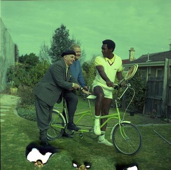 Bill Cosby begins to sit on front seat of tandem whilst Arthur Wilkins and Hubert Opperman look on