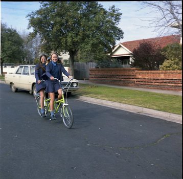 Two school girls riding a tandem bike
