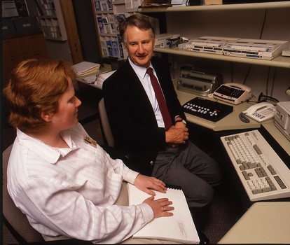 Robin Pleydell sits next to AFB Staff member at her workstation whilst she is reading Braille