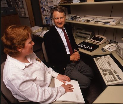 Robin Pleydell sits next to AFB Staff member at her workstation whilst she is reading Braille