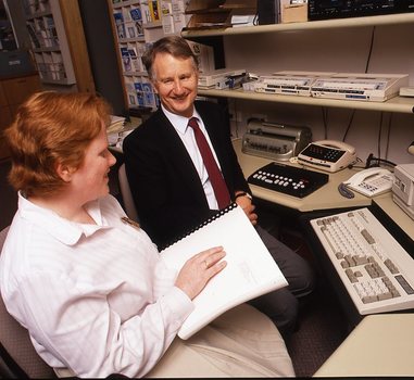 Robin Pleydell sits next to AFB Staff member at her workstation whilst she is reading Braille