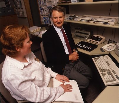 Robin Pleydell sits next to AFB Staff member at her workstation whilst she is reading Braille