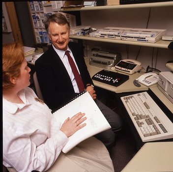 Robin Pleydell sits next to AFB Staff member at her workstation whilst she is reading Braille