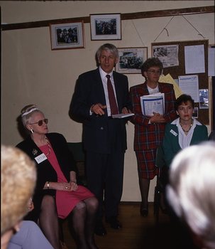 John Cook standing as he talks to a circle of people with a woman standing next to him