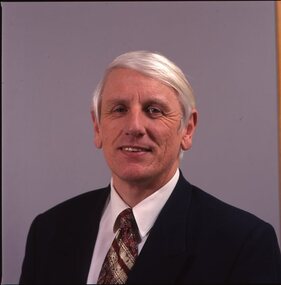 John Cook in dark suit with white shirt and red and gold tie