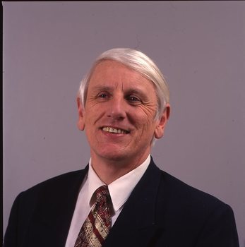 John Cook in dark suit with white shirt and red and gold tie