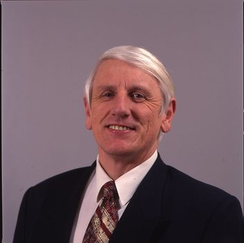 John Cook in dark suit with white shirt and red and gold tie