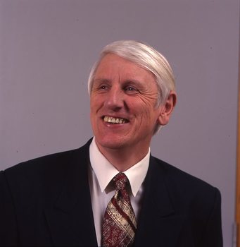 John Cook in dark suit with white shirt and red and gold tie
